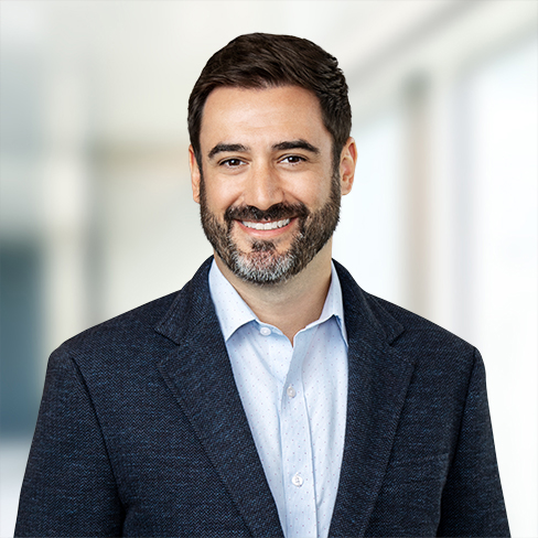 Man with dark hair and beard wearing a blue blazer and light shirt, smiling in a bright, blurred indoor setting—ideal for a corporate law office or lawyers in Chicago seeking a professional look.