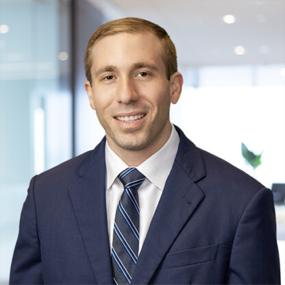 A man in a blue suit and striped tie is smiling while posing in a modern law office environment with glass walls and blurred lights—reflecting the professionalism of leading lawyers in Chicago.
