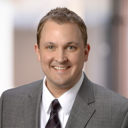 A man in a gray suit, white shirt, and striped tie smiles at the camera against a blurred indoor background, reflecting the professionalism often seen in leading Chicago lawyers.
