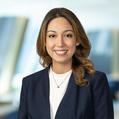 A woman with long brown hair, wearing a navy blazer and white top, smiles at the camera in a modern corporate law office, reflecting the professionalism of Chicago lawyers.