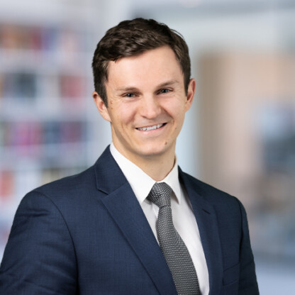 A man in a dark suit, white shirt, and patterned tie smiles in front of a blurred office background, embodying the professionalism of lawyers in Chicago with notable expertise in litigation support.