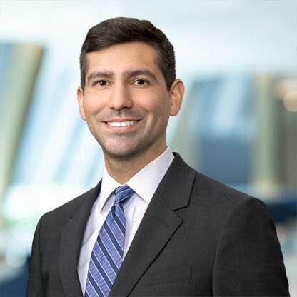 A man in a dark suit, light shirt, and striped tie smiles at the camera with a blurred office background, reflecting the professional atmosphere of top Chicago lawyers.
