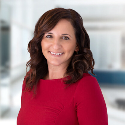 Woman with wavy brown hair wearing a red top, smiling, stands in a brightly lit modern office setting alongside experienced lawyers in Chicago.