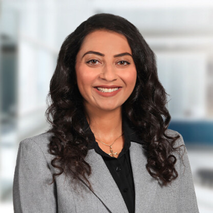 A woman with long, dark, curly hair wearing a gray blazer and black shirt smiles at the camera in a brightly lit corporate law office of Chicago lawyers.