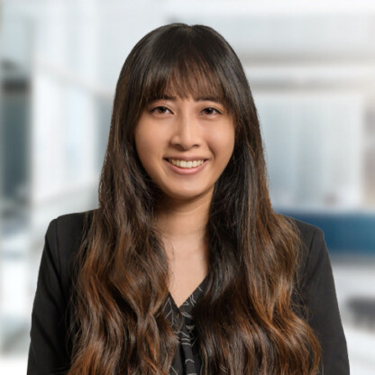 A woman with long, wavy brown hair and bangs, wearing a black blazer, smiles at the camera in a modern law office, representing skilled litigation support for lawyers in Chicago.