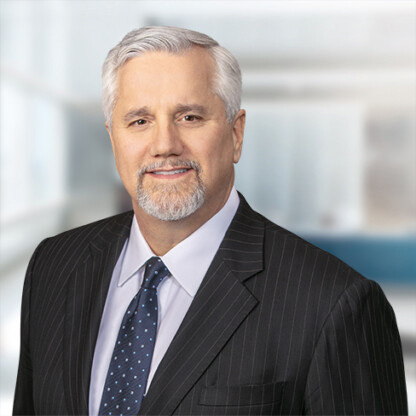 A middle-aged man with gray hair and a goatee, dressed in a dark pinstripe suit, stands in a modern office—exuding the confidence and professionalism of chicago lawyers specializing in intellectual property law.
