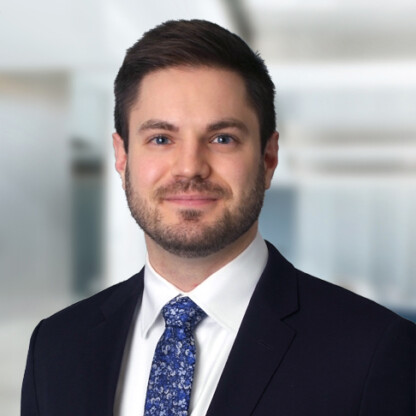 A man in a dark suit, white shirt, and patterned blue tie poses in front of a blurred office background, reflecting his professionalism in intellectual property law.