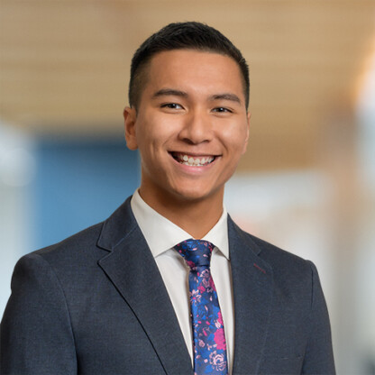 A young man in a suit and floral tie smiles at the camera, embodying the professionalism found in Chicago law offices, with a blurred indoor background.