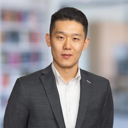 A man wearing a dark suit jacket and white shirt stands in front of a blurred indoor background, reflecting the professional atmosphere often found in corporate law offices.
