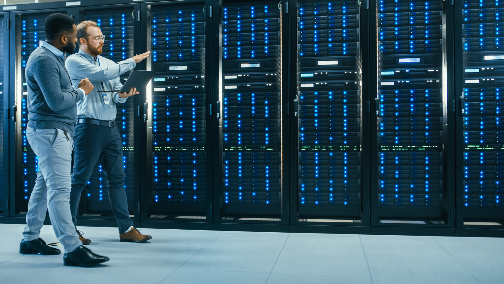 Two men stand in a server room, one holding a laptop and gesturing while discussing the data center equipment—highlighting the technology that chicago lawyers use for litigation support.