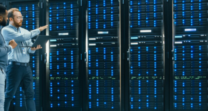 两名男子站在服务器机房里，四周排列着一排排服务器机架。其中一人手持笔记本电脑，指着服务器讨论知识产权法律管理的解决方案。