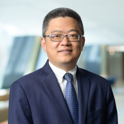 A man in a navy suit, white shirt, and patterned tie stands indoors against a blurred background, looking at the camera and smiling slightly—reflecting the professionalism of top chicago lawyers.