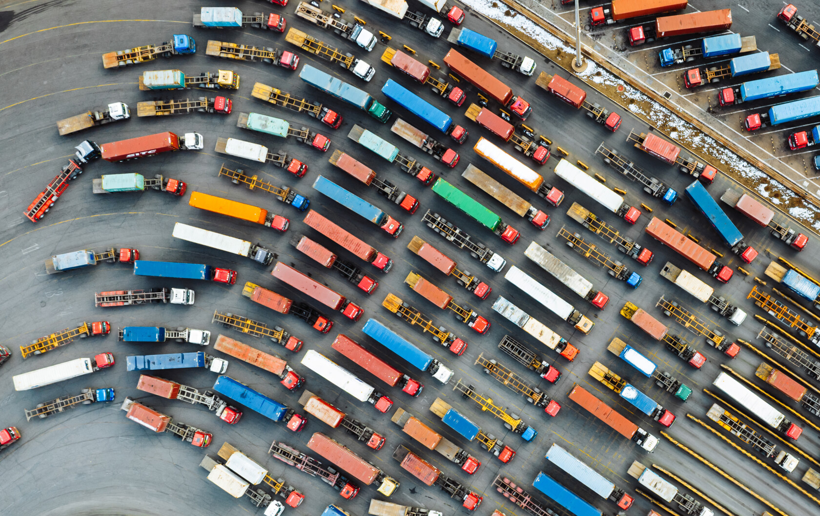 Aerial view of numerous colorful trucks and trailers parked in organized rows on a large paved lot.