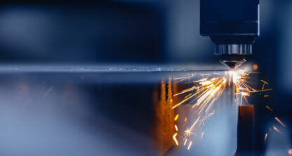 Close-up of a CNC laser cutting machine emitting sparks as it cuts through a sheet of metal in an industrial setting.