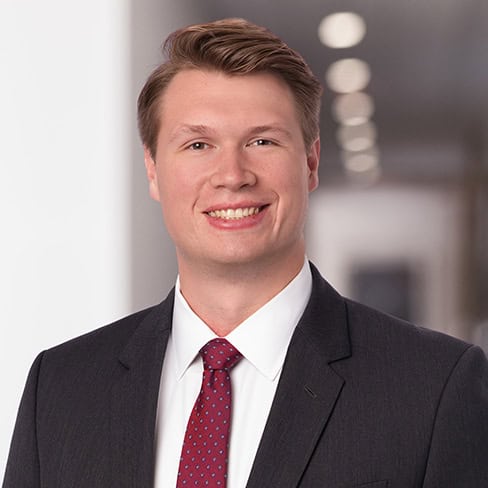 Young professional male in formal business suit smiling in office setting.