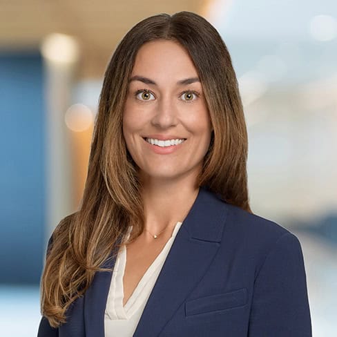 Woman in professional business attire smiling at the camera in office setting.