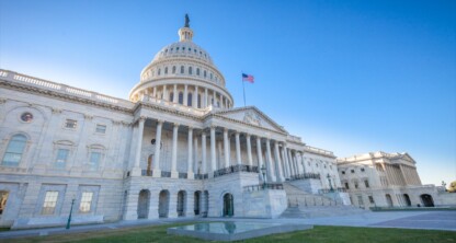 The United States Capitol building in Washington, D.C., under a clear blue sky, with the American flag flying in front.
