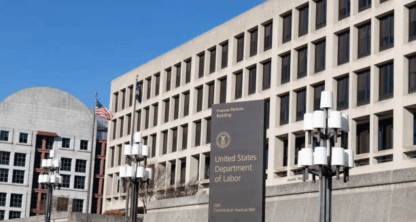 United States Department of Labor building with signage, American flags, and modern architecture on a clear day.